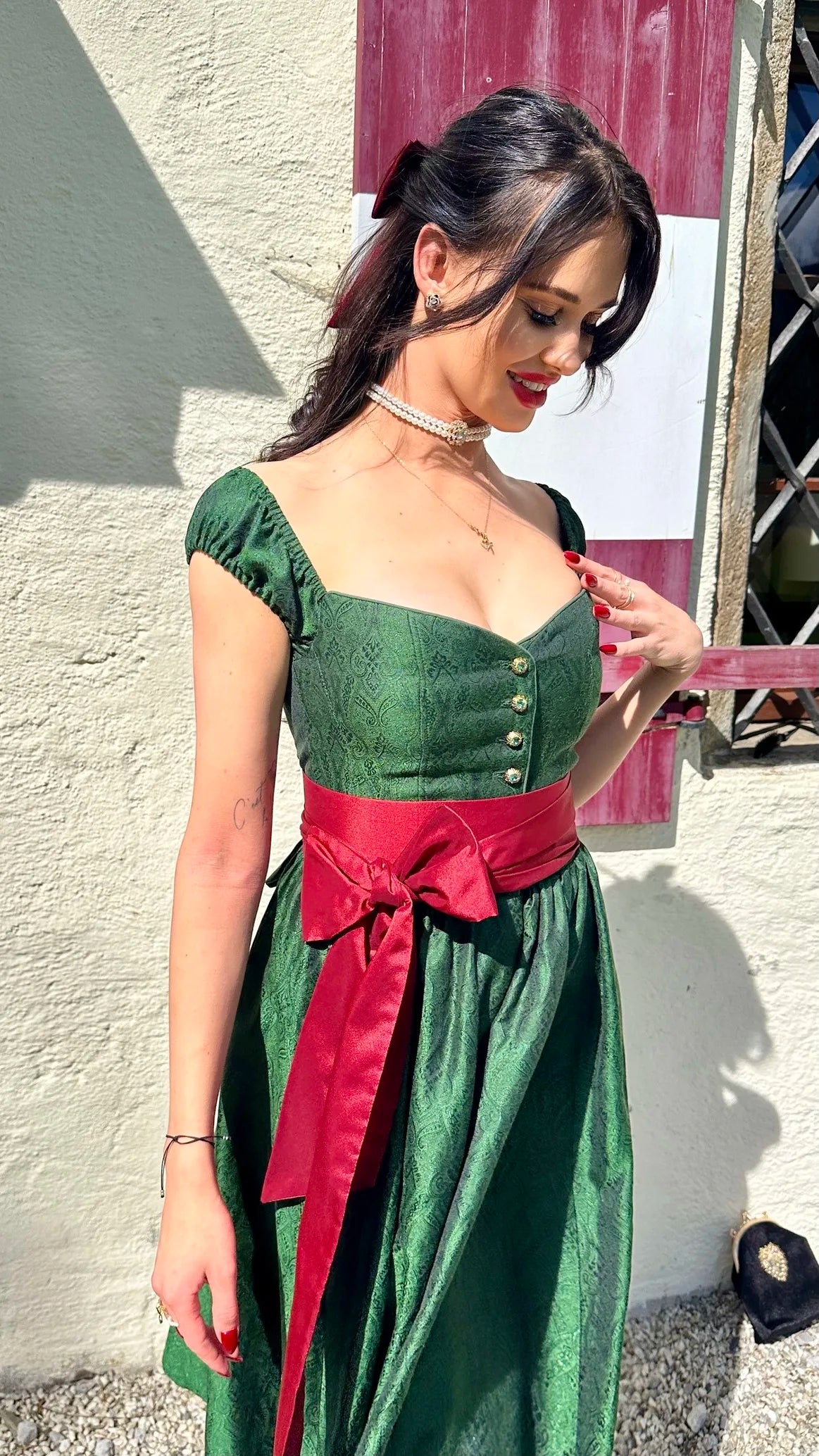 Smaragd grünes Dirndl Sissi Smaragd Edition mit roter Schleife an Frau getragen (Vorderansicht) – elegante Trachtenmode in stilvoller Präsentation.